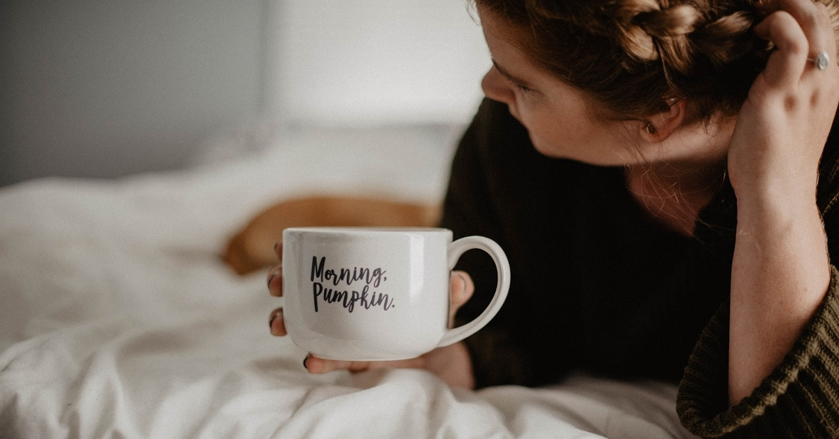 Woman lying in bed with a white coffee mug