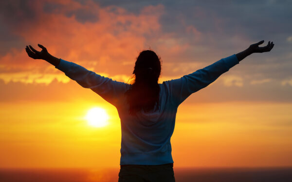 Silhouette of woman with raised arms against a sunset background