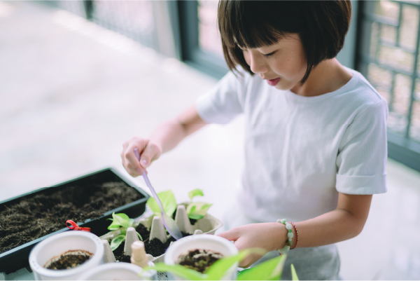 A child scooping dirt into a planter with a spoon