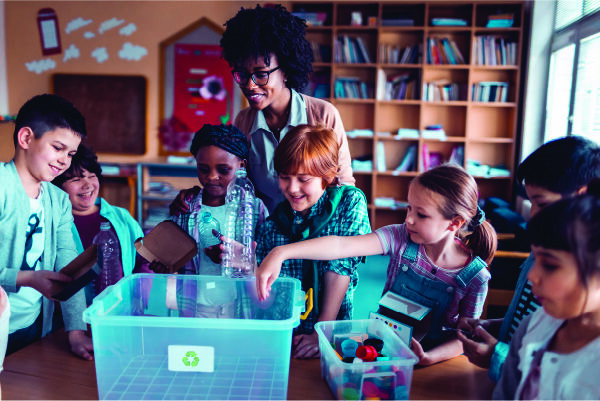 A woman watching over a group of children as they learn to recycle