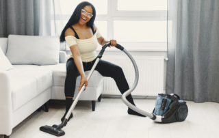 Woman vacuuming while smiling and sitting on the couch