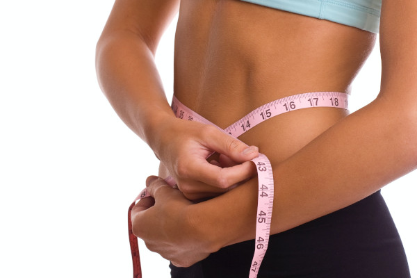 Close-up of pink tape measure wrapped around a woman's waist