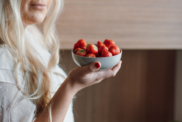 Blonde woman in a white blouse holding a bowl of strawberries