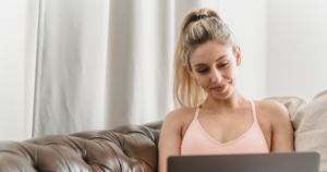 Woman in pink activewear using a laptop on a brown leather couch