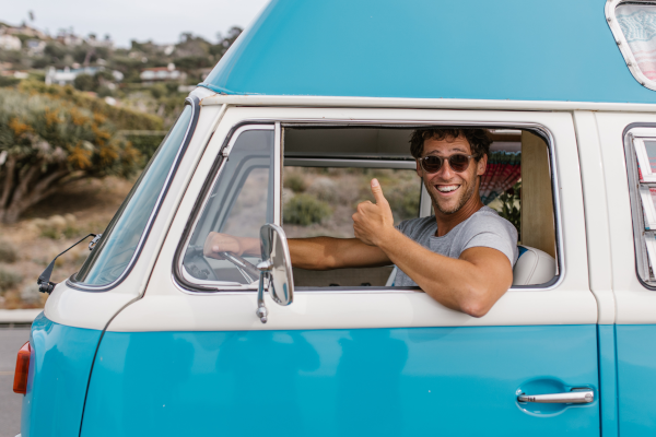 Man in sunglasses giving a thumbs up while driving a bright blue van